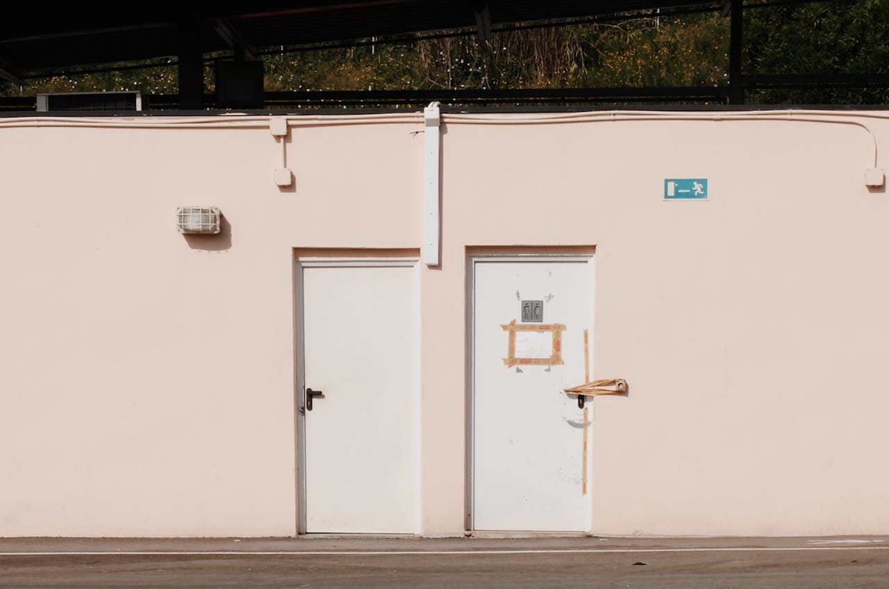 A minimalist image of an exterior wall with two doors and an emergency exit sign, creating a modern urban feel.